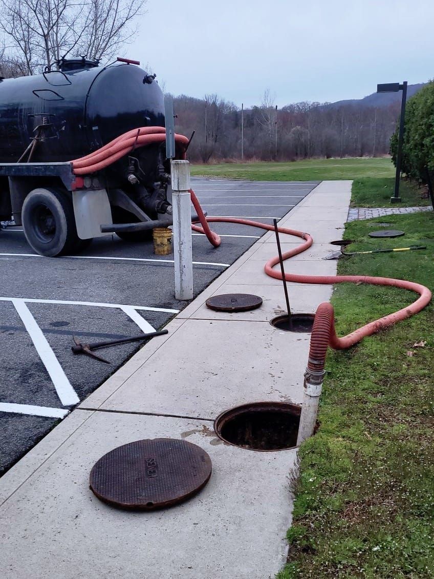 A septic tank is being pumped into a manhole in a parking lot