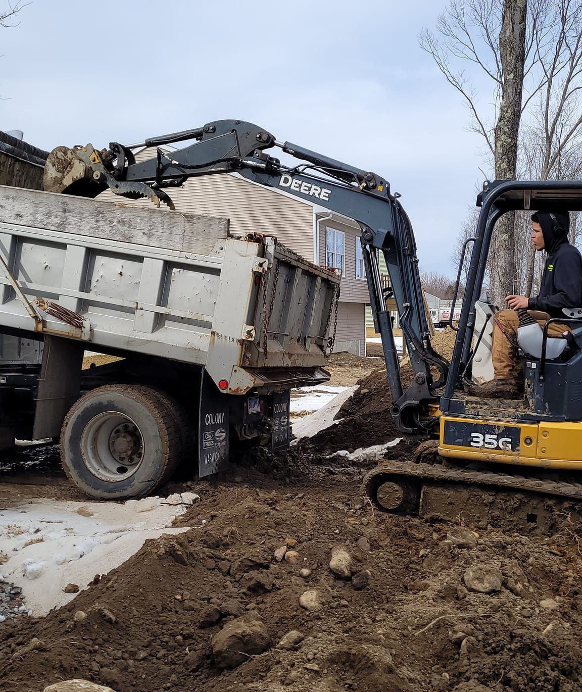 A dump truck is being loaded with dirt by an excavator.