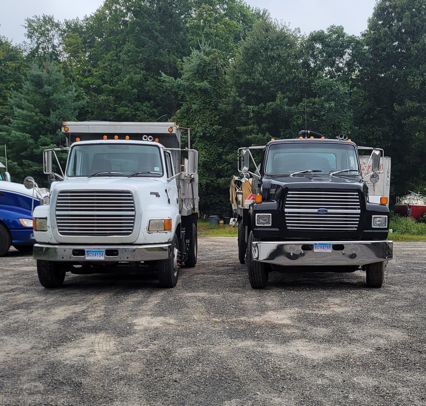 Two dump trucks are parked next to each other in a gravel lot