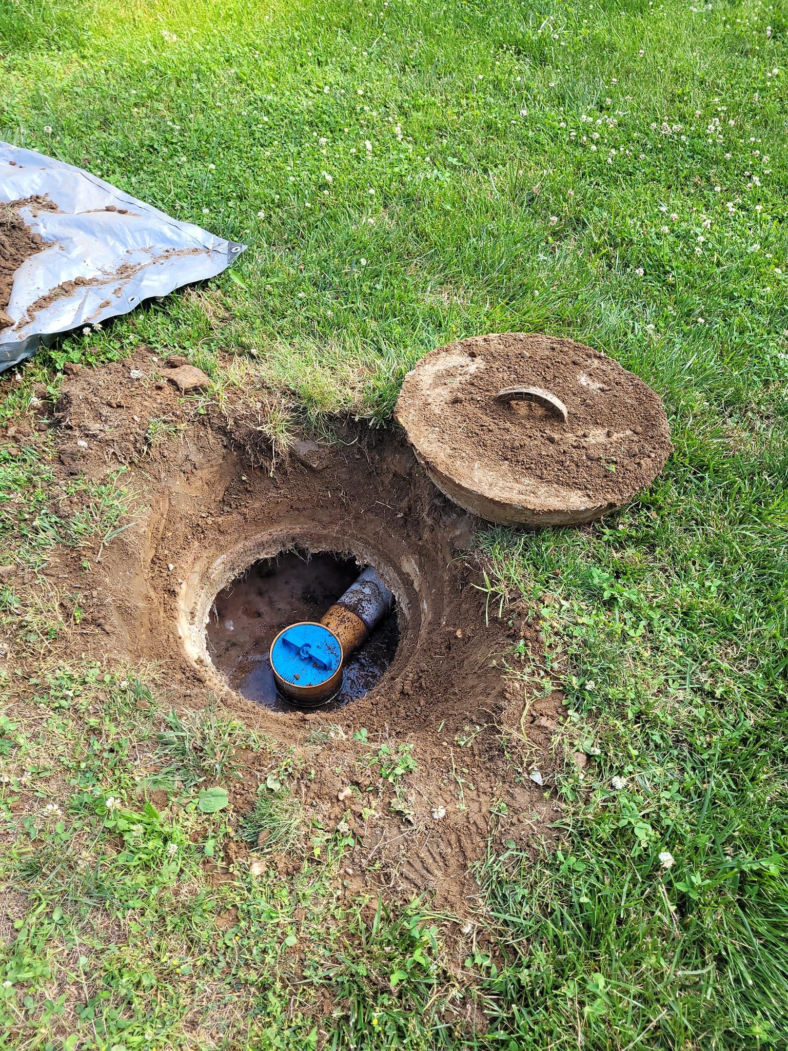 A manhole cover is sitting in the middle of a hole in the grass.