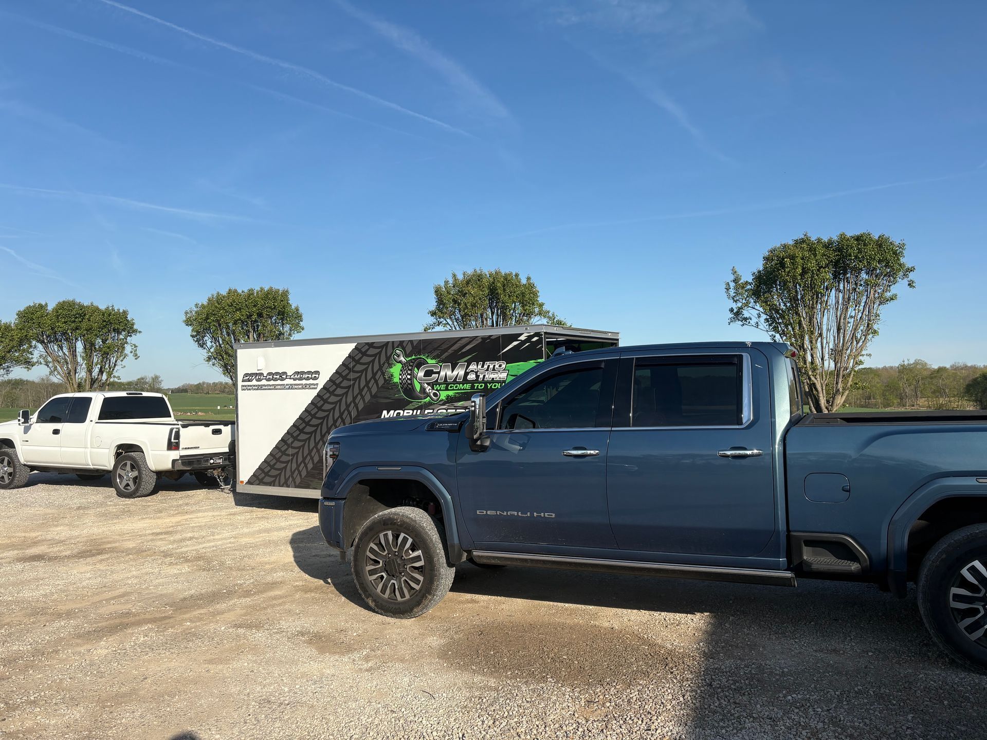Dark blue pickup truck parked on gravel beside a white SUV under a clear blue sky