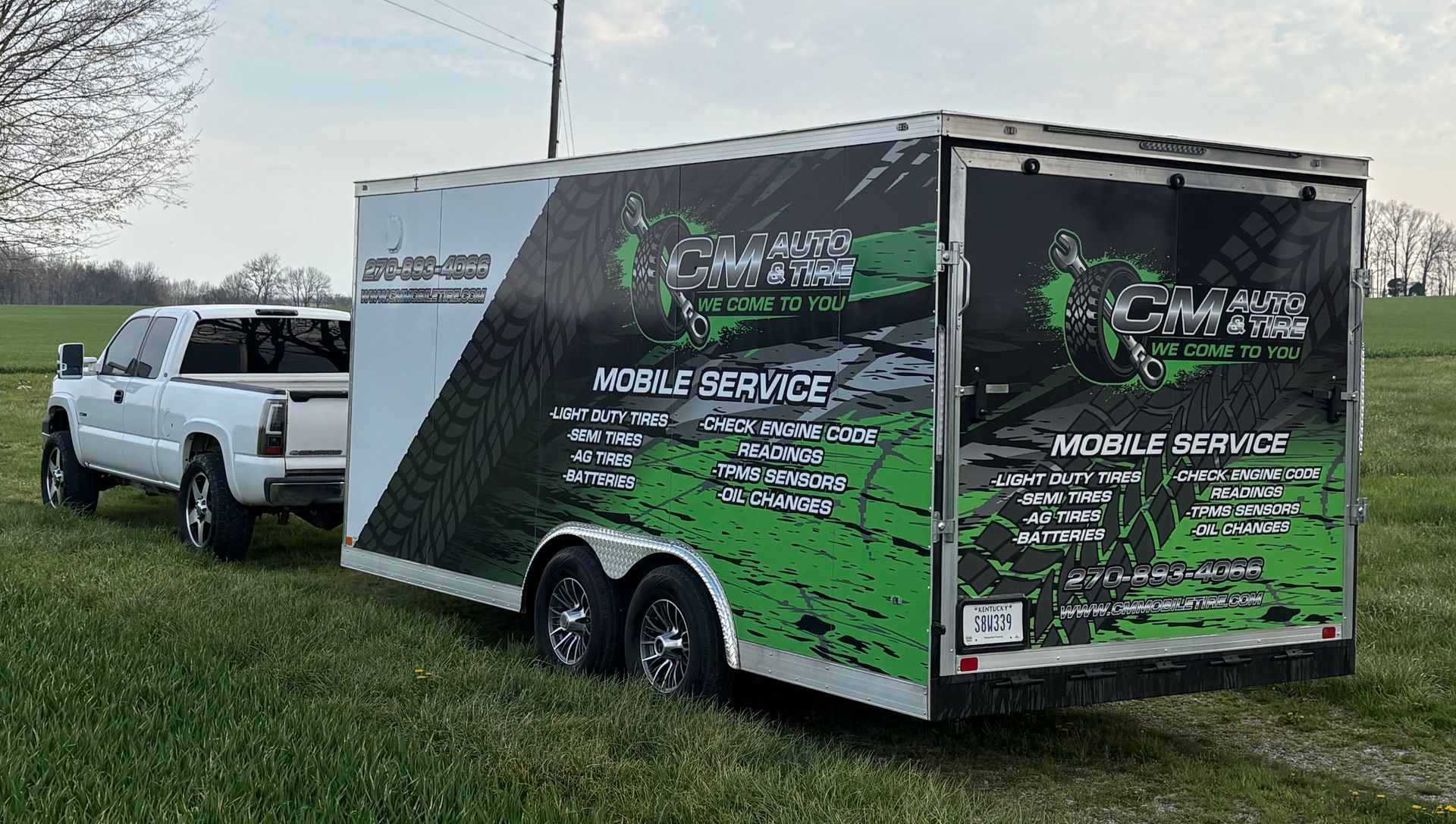 White pickup truck towing a black-and-green enclosed trailer in a grassy field outdoors