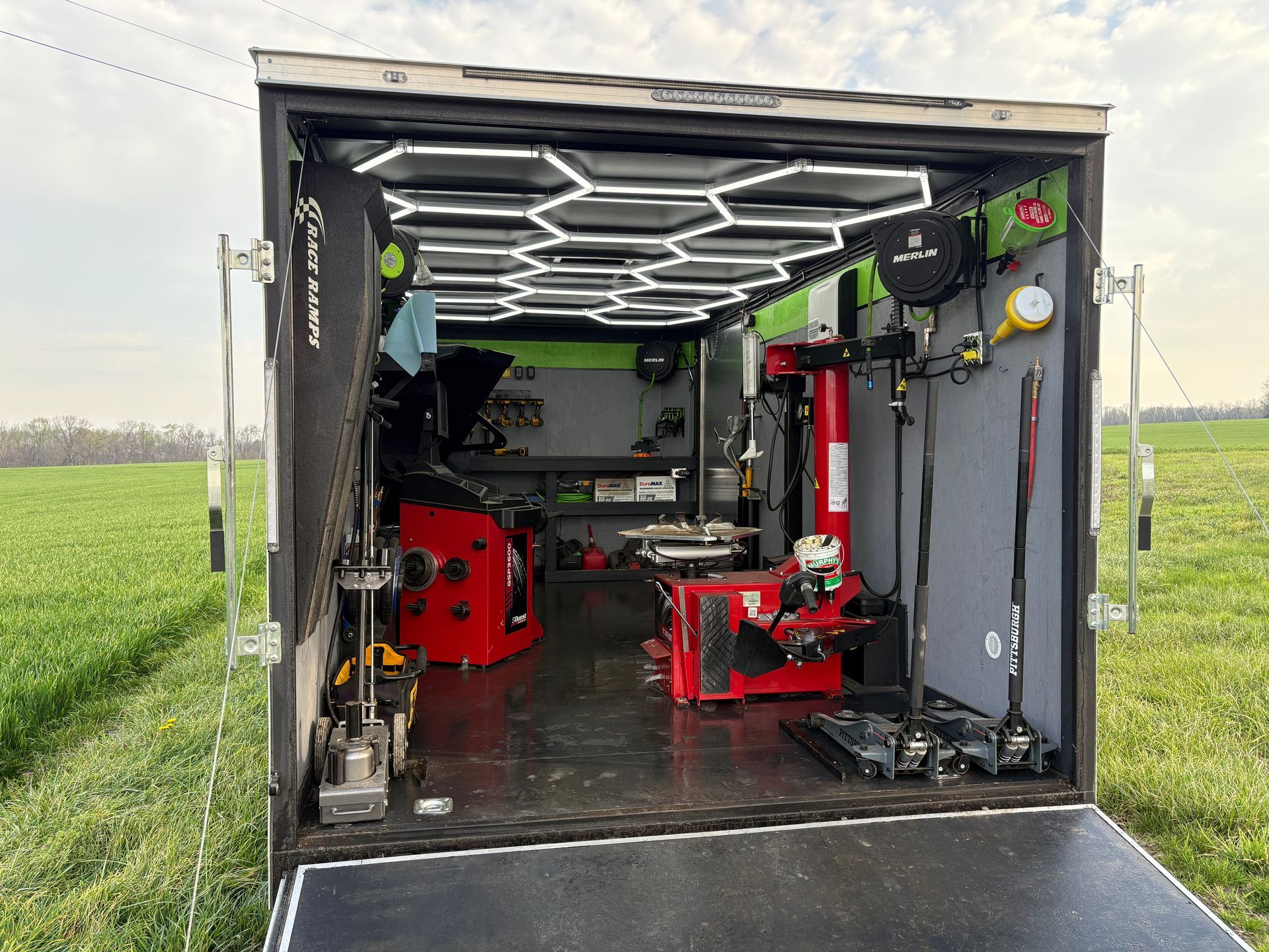 Open truck trailer workspace with red machinery and LED ceiling lights, parked in a green field