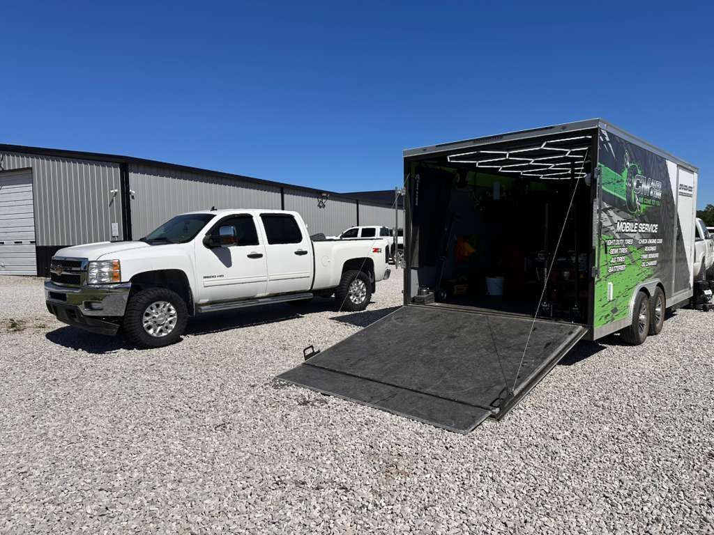 White pickup truck beside open cargo trailer ramp in a gravel lot under blue sky