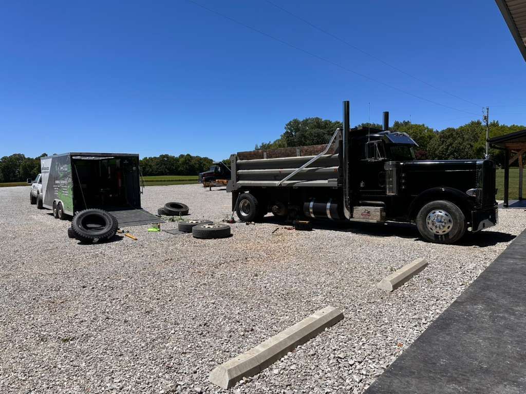 Two dump trucks and loose tire in a gravel lot under a clear blue sky