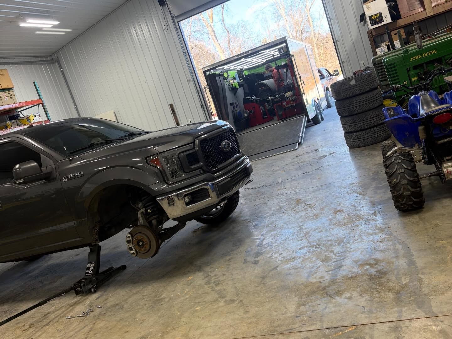 Dark pickup truck on jacks in a workshop, with tires and tools stacked nearby.