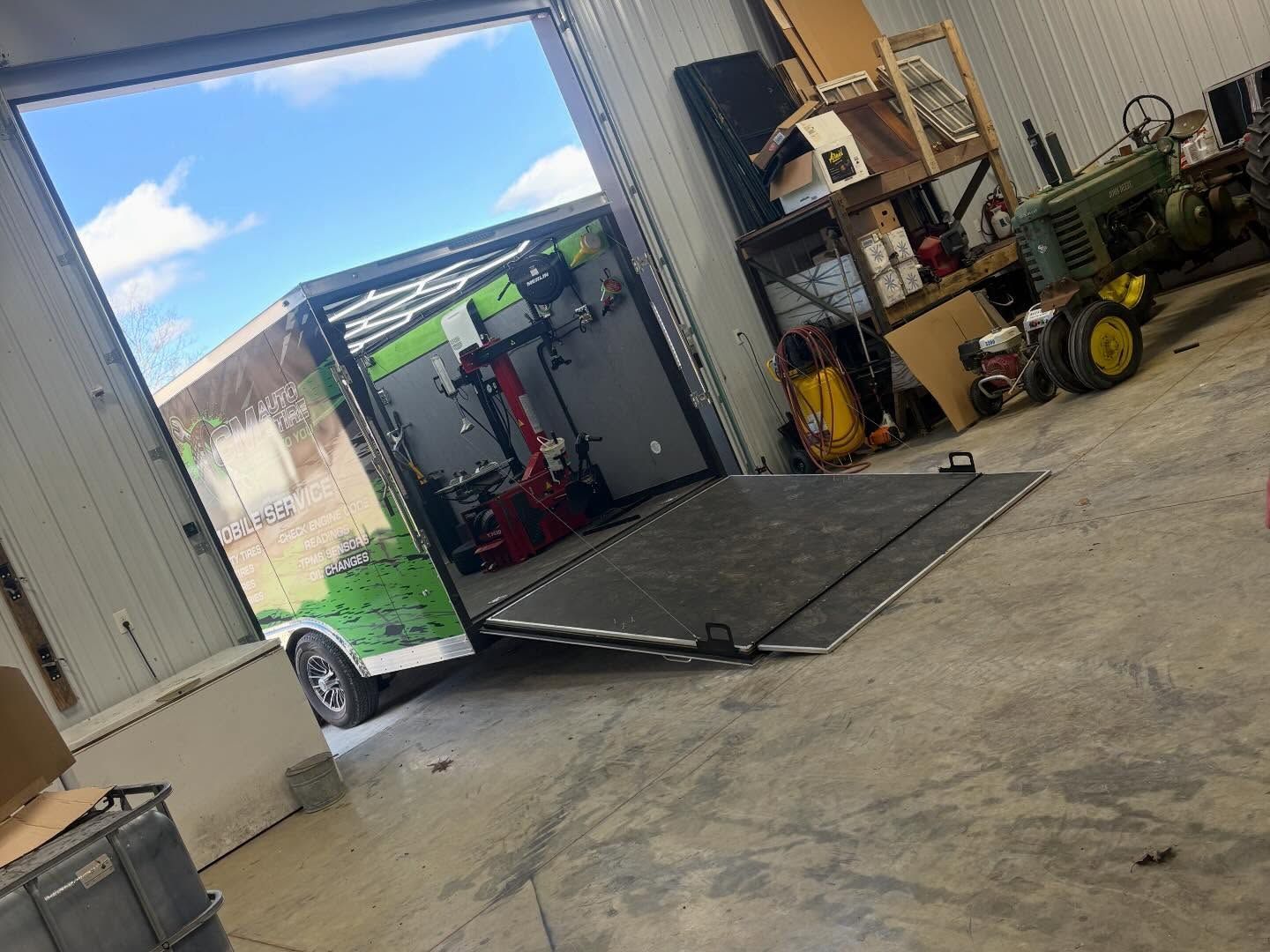 Tilted enclosed trailer in a workshop, with tools and equipment visible inside and around it.