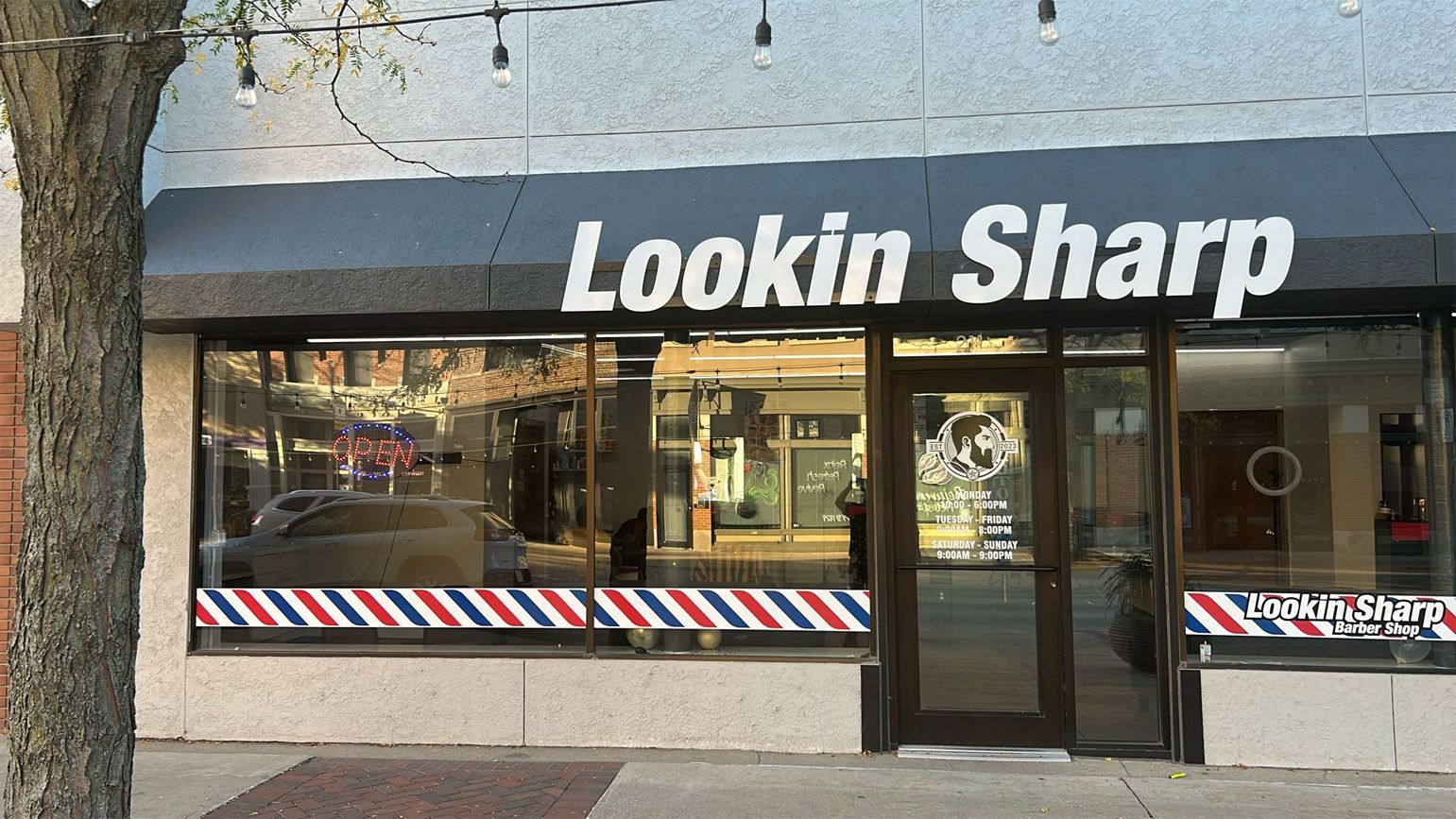 Barbershop 'Lookin Sharp' storefront with black awning, glass windows, and red, white, and blue stripes.