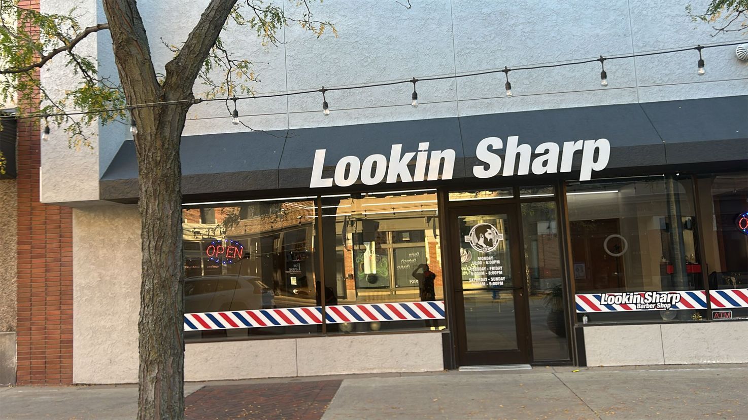 Lookin Sharp barbershop storefront with awning. Sign is black with white text, red/white/blue stripes on the facade.