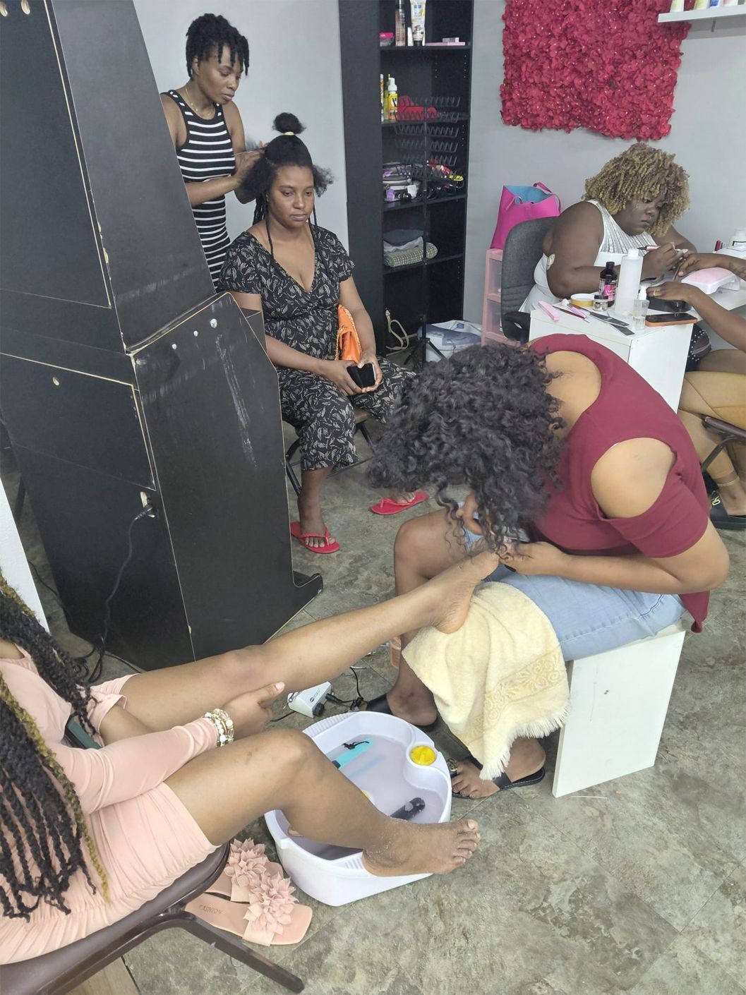 A salon scene: clients getting pedicures and hair styled. Women in a brightly lit room.