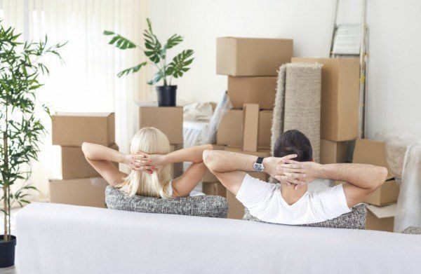 Two people relaxing on a couch in a room with moving boxes and plants, packing for a move