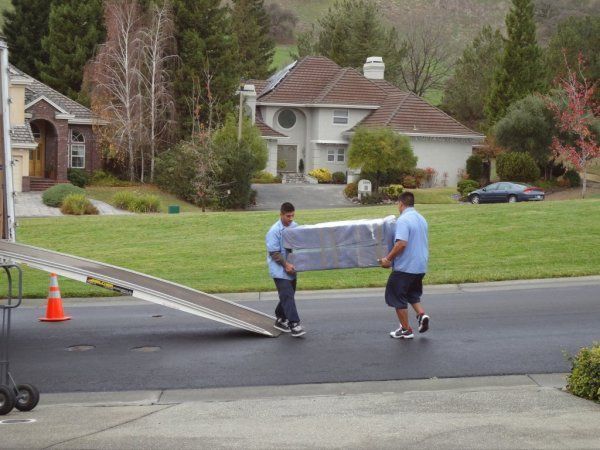 Two men carrying a large wrapped item across a street in a suburban neighborhood