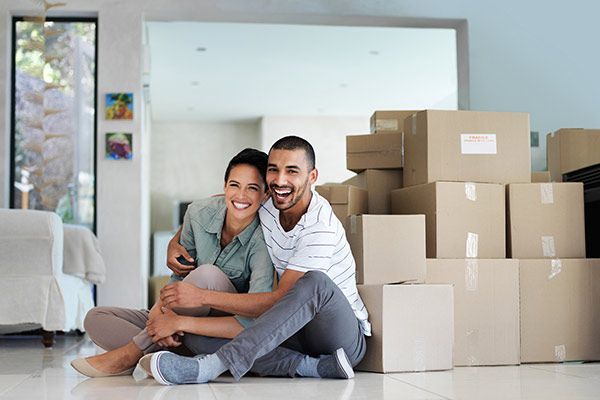 Smiling couple sitting on the floor in a bright room beside stacked moving boxes