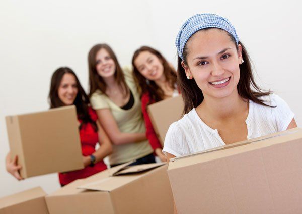 Four people packing cardboard boxes in a bright room, with one smiling in the foreground