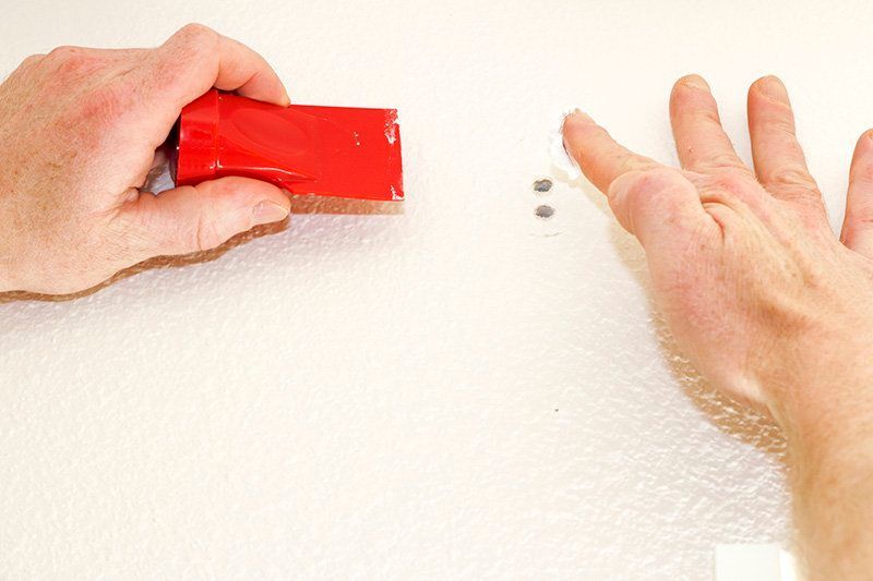 Hands holding a red wall patch and smoothing a white textured wall surface
