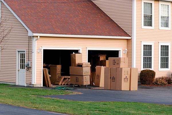 Packed cardboard boxes outside an open garage in a suburban house driveway