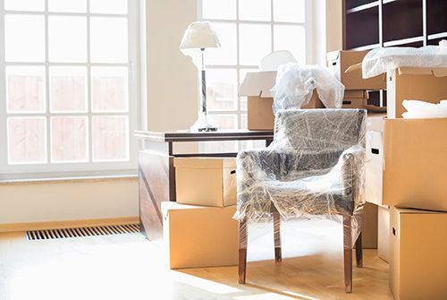 Wrapped armchair and stacked moving boxes in a sunlit room with large windows