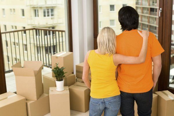 Couple standing by moving boxes on an apartment balcony, looking out over the building complex