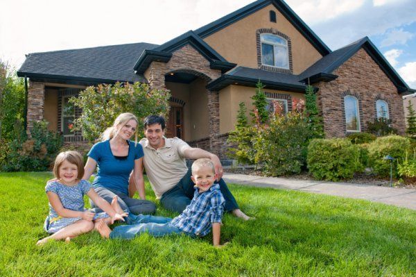 Family sitting on grass in front of a suburban house and smiling at the camera