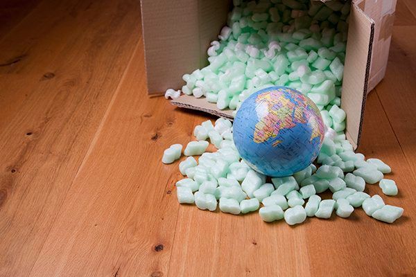 Globe spilling from a cardboard box onto wooden floor, surrounded by packing peanuts