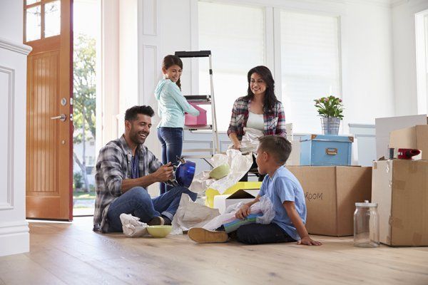 Family unpacking boxes in a bright living room, with children and adults smiling amid moving supplies.
