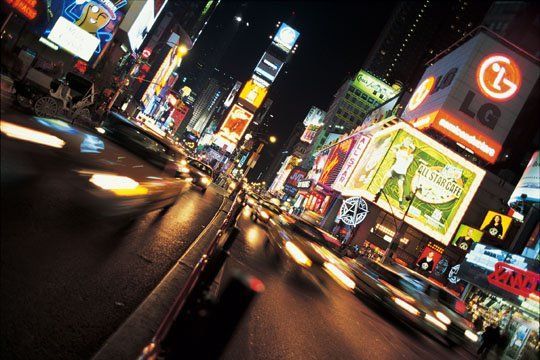 Blurred neon-lit city street at night with bright billboards and light trails from traffic