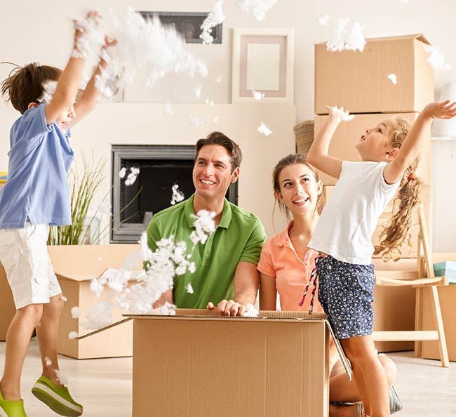 Family celebrating in a living room with moving boxes as children toss packing paper around a smiling couple