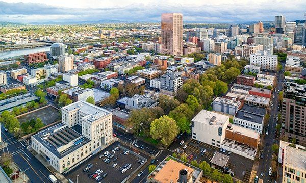 Aerial view of a city center with mid-rise buildings, tree-lined streets, and a tall tower under a cloudy sky