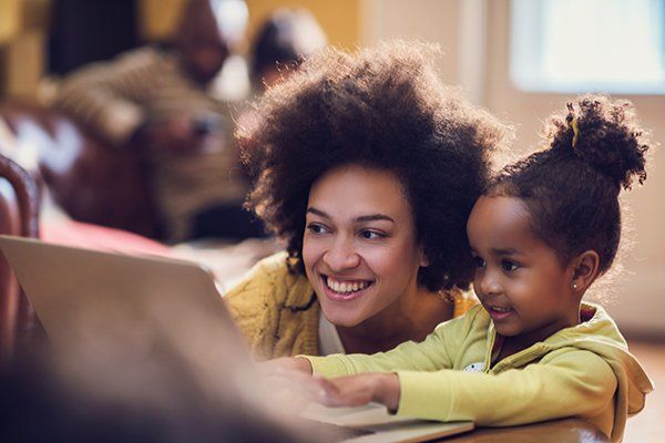 Smiling woman and child using a laptop together at a table