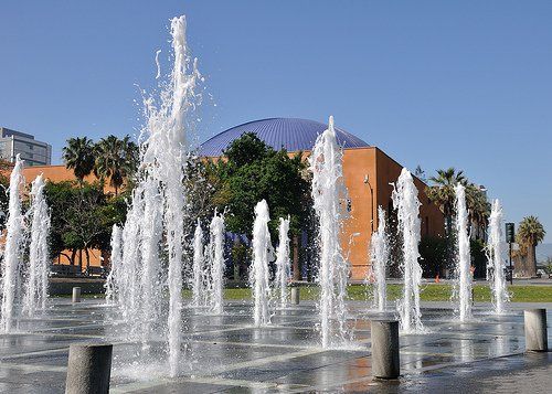 Outdoor fountain jets spraying water in front of a modern building under a clear blue sky