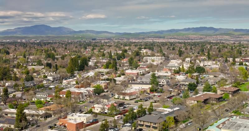 Aerial view of a suburban neighborhood with trees, houses, and mountains in the distance.