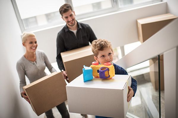 Family carrying moving boxes up a staircase, with a child holding a toy in the foreground