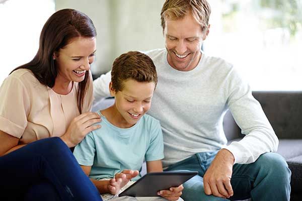 Family sitting on a couch, smiling and using a tablet together