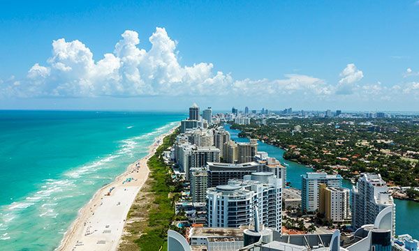 Aerial view of a turquoise beach and ocean beside high-rise waterfront buildings under a blue sky