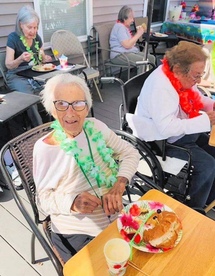 Seniors seated at a festive table, smiling with leis and dessert in a bright community room.