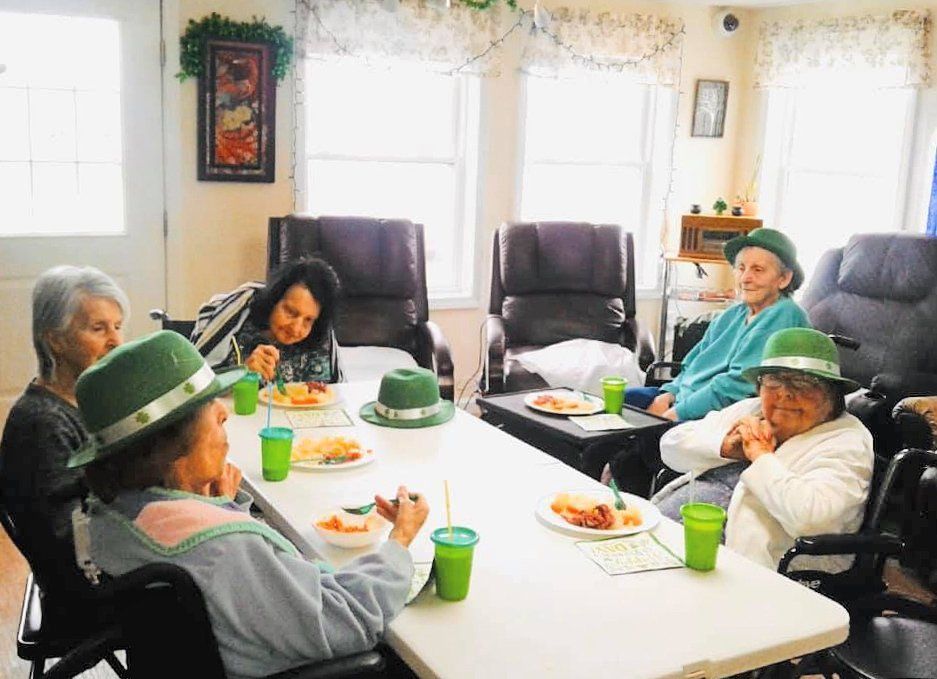 People seated around a table eating in a bright living room with green hats and cups