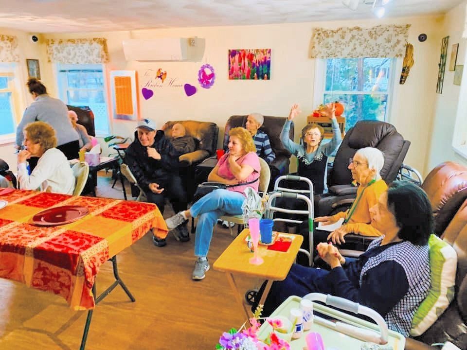 People seated in a cozy living room, chatting around tables with colorful decorations and walkers nearby