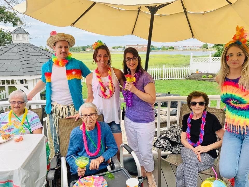 People posing outdoors under a yellow umbrella at a festive gathering, wearing colorful leis and hats