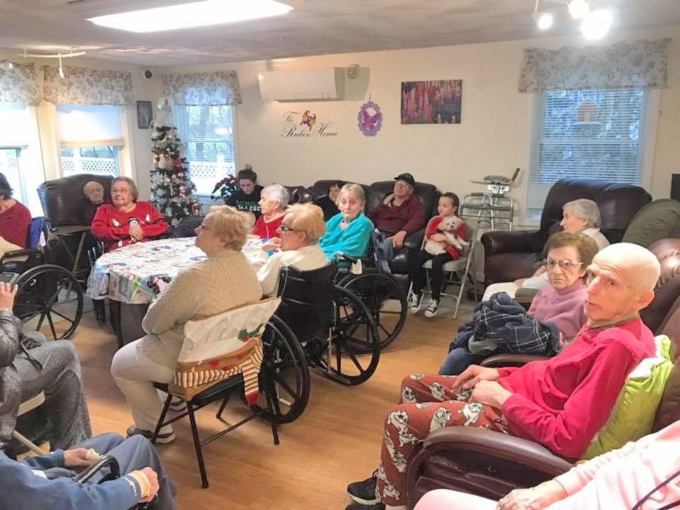 Residents seated in a bright common room, chatting in a circle of chairs and wheelchairs