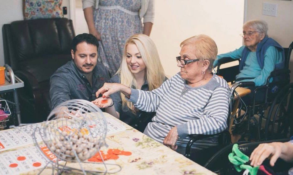 People playing a tabletop game with cards and tokens at a table, in a care home lounge