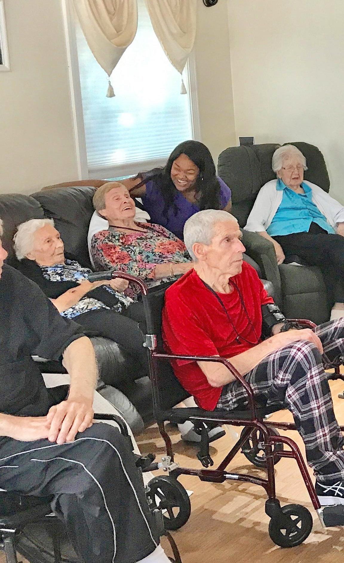 People seated in a living room, including several in wheelchairs, chatting and resting.