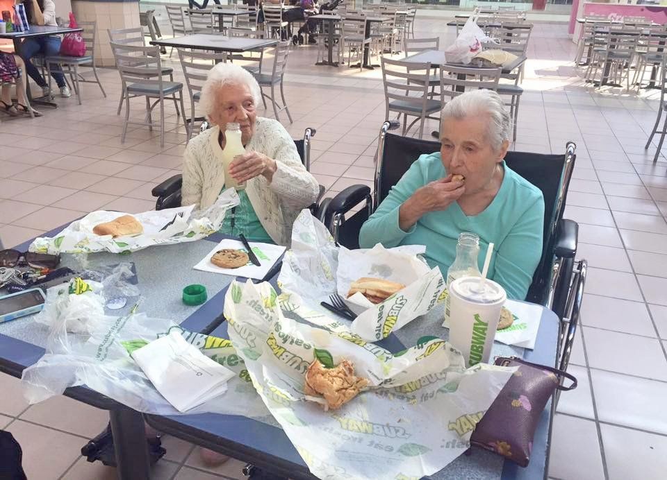 Two people eating at an outdoor patio table with food wrappers and trays.