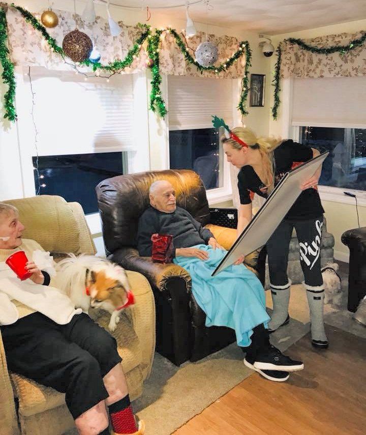 People opening holiday gifts in a decorated living room with a dog on a couch