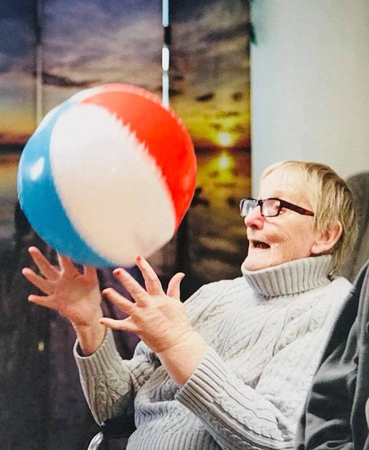 Woman in a gray sweater reaching for a red, white, and blue beach ball indoors