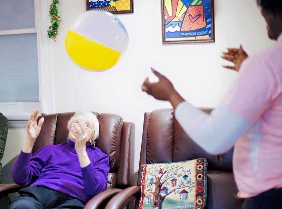 People tossing a yellow-and-white beach ball to an older person seated in a living room
