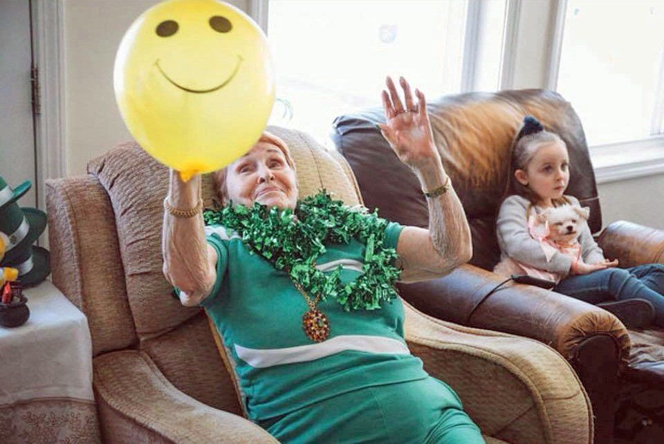 Woman on a couch holds a smiley balloon beside a child sitting nearby in a living room.