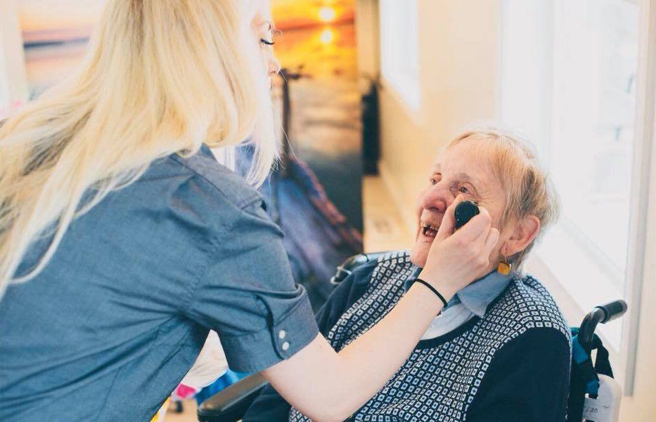 Caregiver checks elderly man’s mouth in a bright care facility