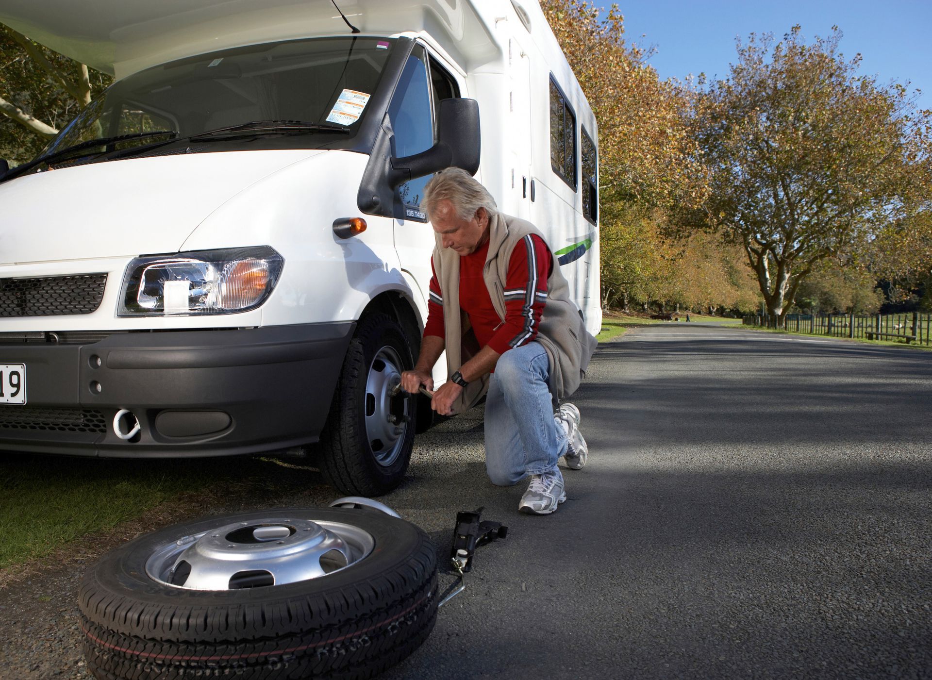 Man changing a tire on a white RV on a paved road; spare tire on the ground.
