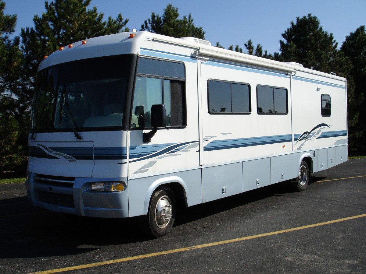 Light blue and white RV parked on pavement, with an awning extended.