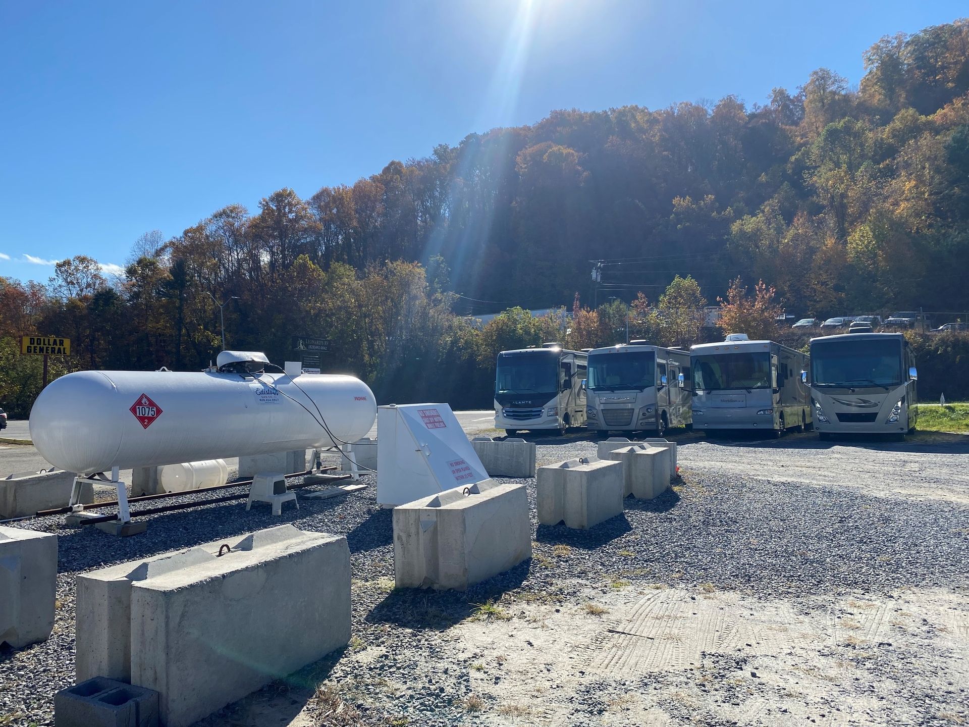 Propane tank and RVs in a gravel lot on a sunny day with trees in the background.